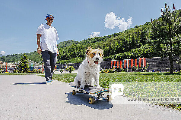 Smiling man with dog sitting on skateboard in park