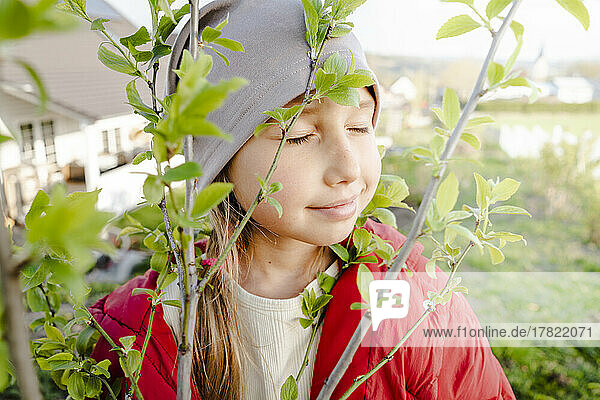 Smiling girl with eyes closed by plant in garden