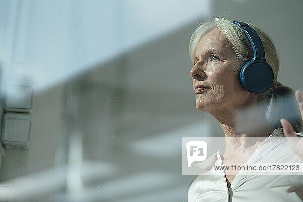 Smiling senior woman listening music through wireless headphones