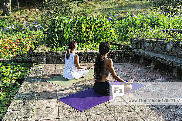 Girl sitting with yoga coach meditating in park