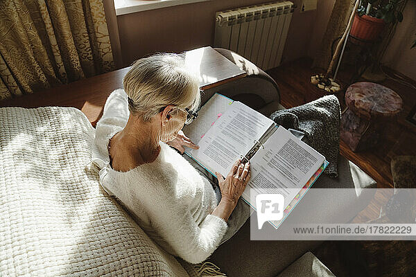 Senior woman reading document sitting on sofa at home