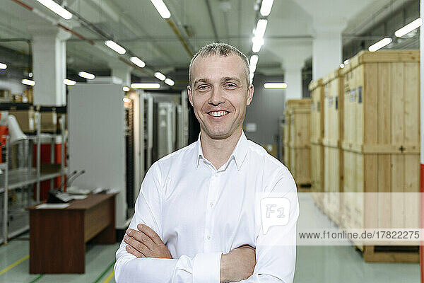 Smiling businessman with arms crossed standing in warehouse