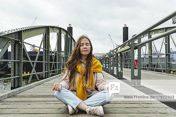 Young woman with eyes closed meditating on footbridge