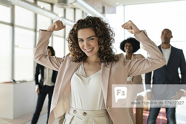 Cheerful businesswoman flexing muscles at office