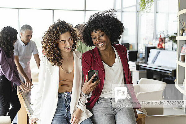Happy businesswomen sharing smart phone at office