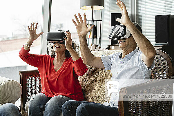 Happy business colleagues wearing virtual reality simulator sitting on sofa gesturing in office