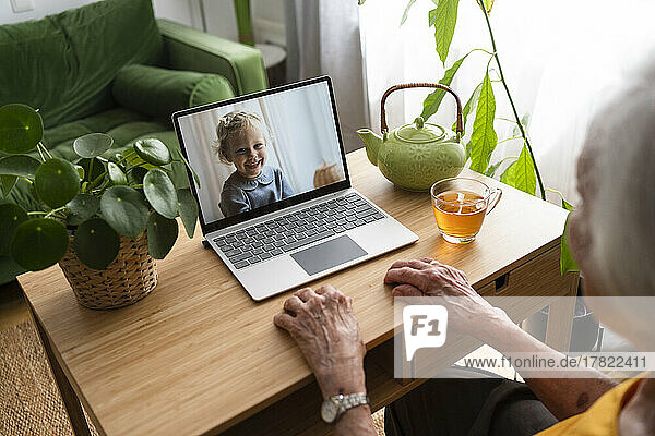 Senior woman talking on video call with granddaughter through laptop