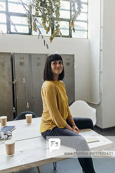 Smiling businesswoman sitting on desk at workplace
