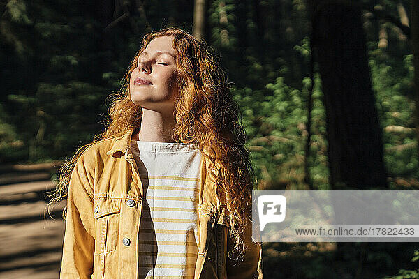 Woman with eyes closed enjoying sunlight in forest