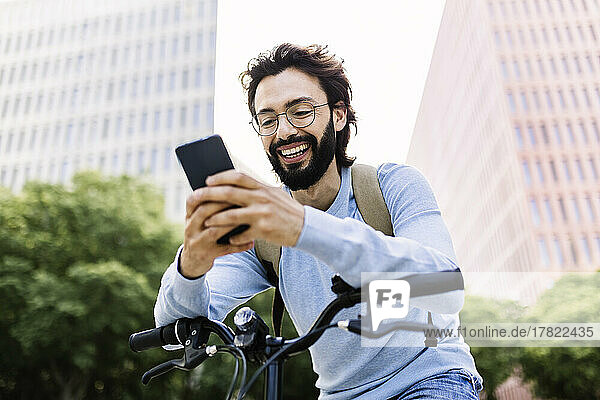 Smiling man using mobile phone leaning on bicycle