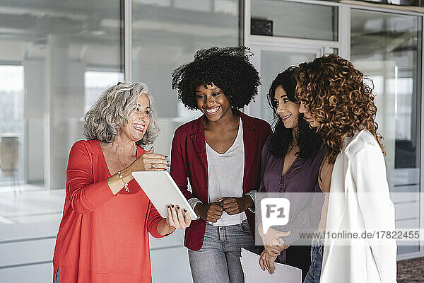 Happy businesswoman with colleagues discussing over tablet PC