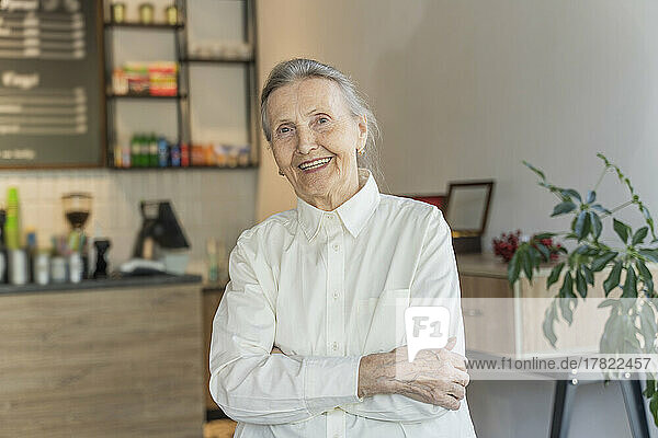 Happy senior woman with arms crossed standing in cafe
