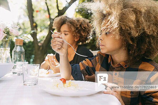 Boy with sister eating lunch at dining table in yard