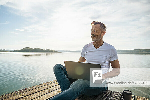 Happy freelancer with laptop and enjoying view from pier