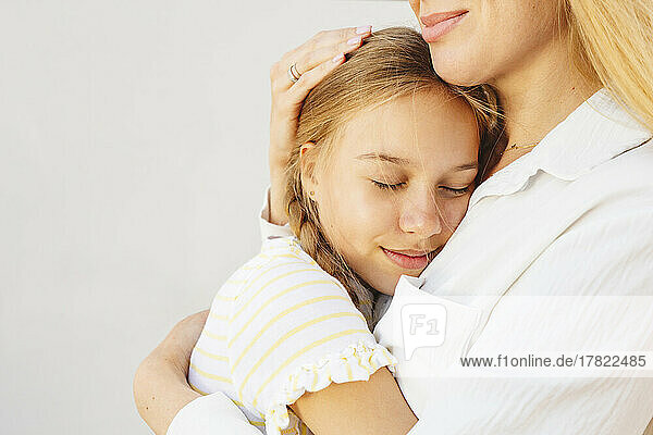 Smiling woman hugging daughter in front of wall