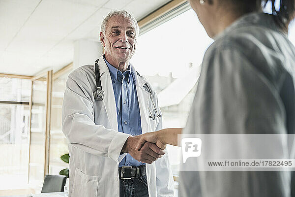 Glücklicher Arzt schüttelt dem Patienten in der Klinik die Hand