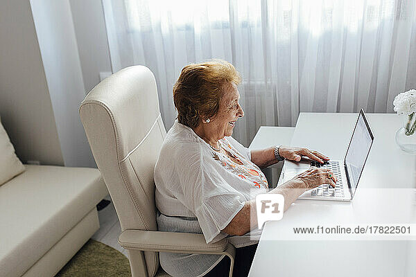 Lächelnde ältere Frau mit Laptop am Tisch sitzend