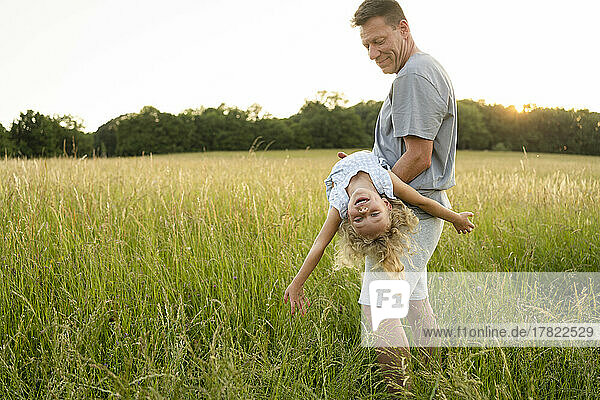 Smiling father carrying daughter enjoying at field