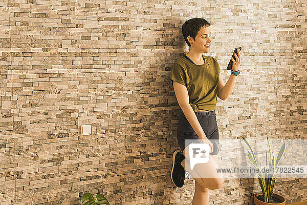 Smiling woman using mobile phone standing in front of wall