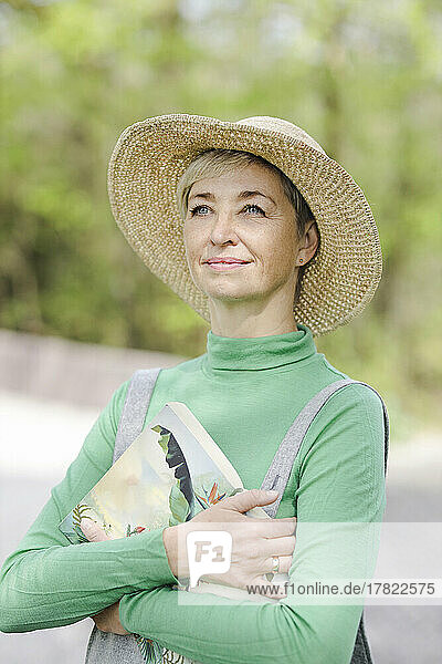 Thoughtful smiling woman wearing hat standing with book