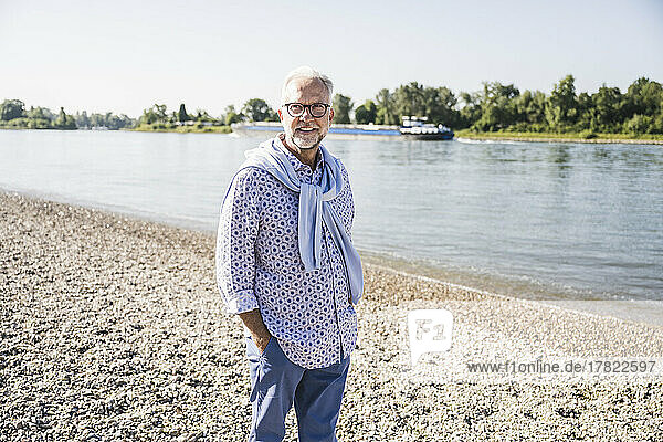 Smiling senior man standing with hand in pocket at riverbank