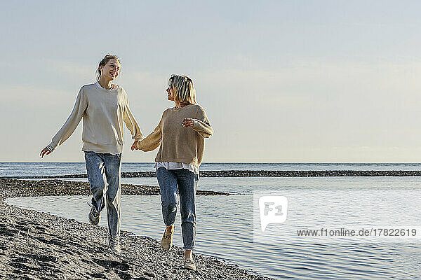 Mutter und Tochter laufen Händchen haltend am Strand