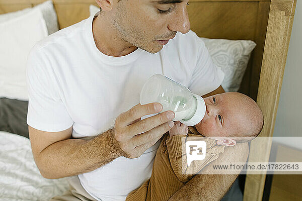 Father feeding milk to baby boy with bottle at home