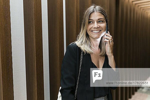 Smiling businesswoman talking on mobile phone at hotel corridor