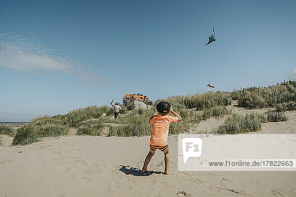 Boy flying kite with father on sunny day at beach