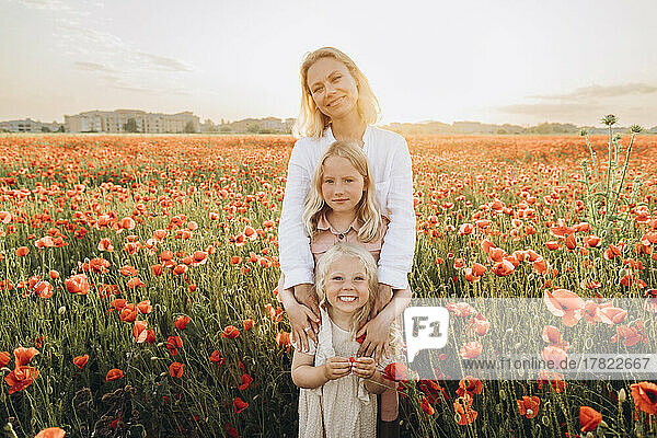 Lächelnde Mutter mit Töchtern  die im Mohnfeld stehen
