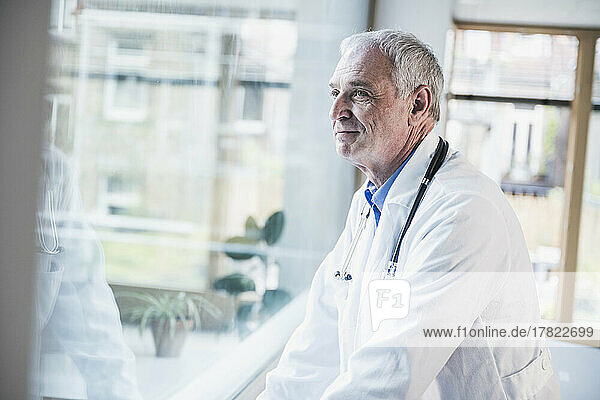 Smiling doctor looking through window at hospital