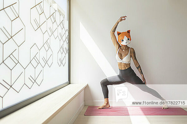 Woman with hand raised wearing animal mask doing yoga in studio