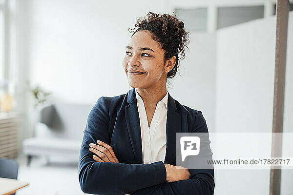 Happy businesswoman with arms crossed looking away in office