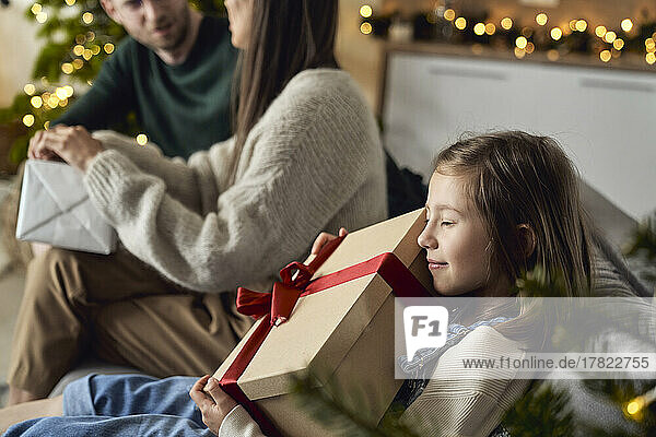 Smiling girl embracing gift box sitting by parents at home