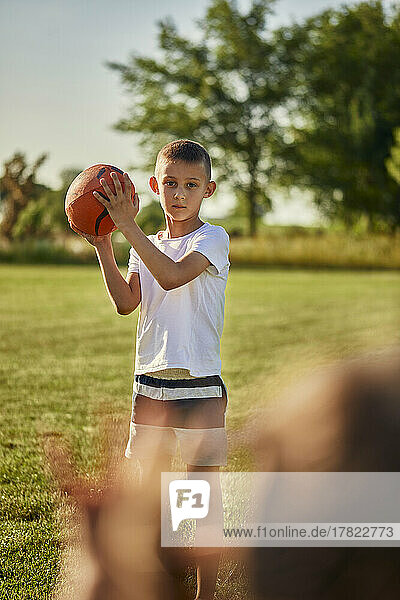 Junge hält Rugbyball und steht an einem sonnigen Tag auf dem Sportplatz