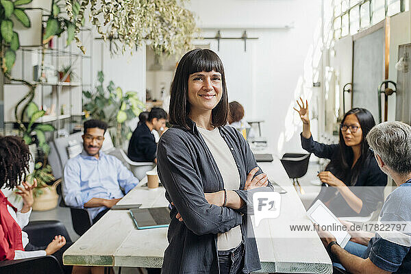 Smiling businesswoman with arms crossed with colleagues in office