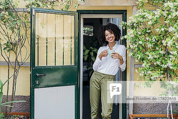 Smiling young businesswoman having coffee at doorway
