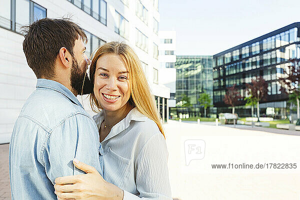 Cheerful blond woman with boyfriend standing in front of building
