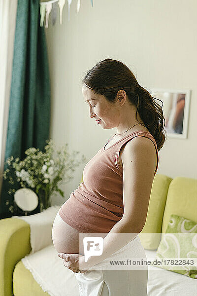 Pregnant woman holding abdomen standing by sofa at home