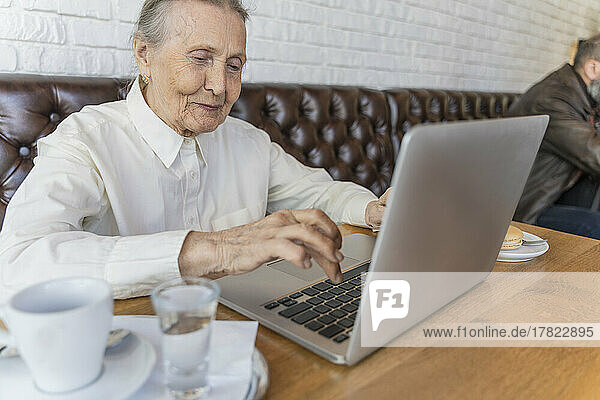 Smiling senior woman using laptop in cafe