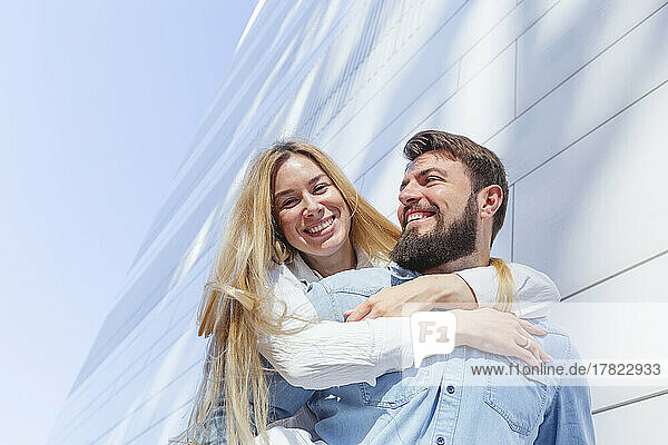 Happy man giving piggyback ride to woman in front of wall