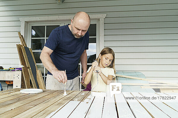 Father and daughter painting planks in back yard