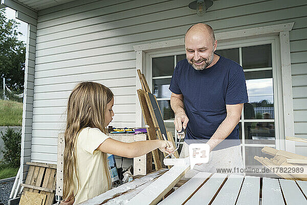 Smiling man painting planks with daughter in back yard