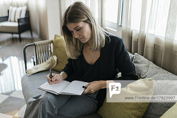 Businesswoman writing in dairy sitting on sofa at hotel