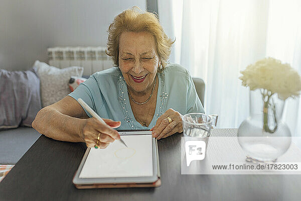 Happy senior woman using tablet PC sitting at table