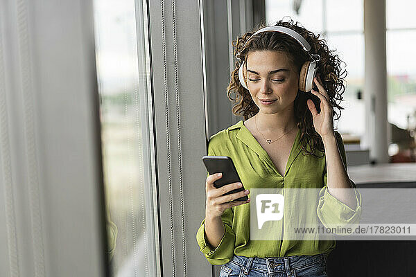 Businesswoman wearing headphones listening music through smart phone at office