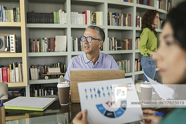 Reifer Geschäftsmann mit Brille sitzt vor Bücherregal