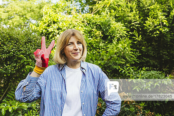 Lächelnde Frau zeigt im Garten ein Siegeszeichen