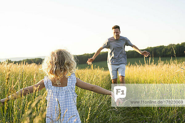 Mature man running towards daughter standing with arms outstretched at field
