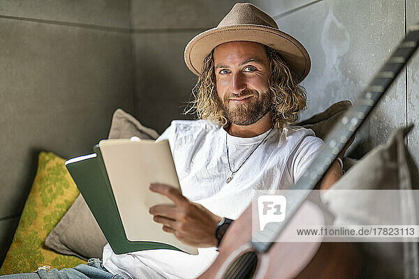 Smiling guitarist with book and guitar at home